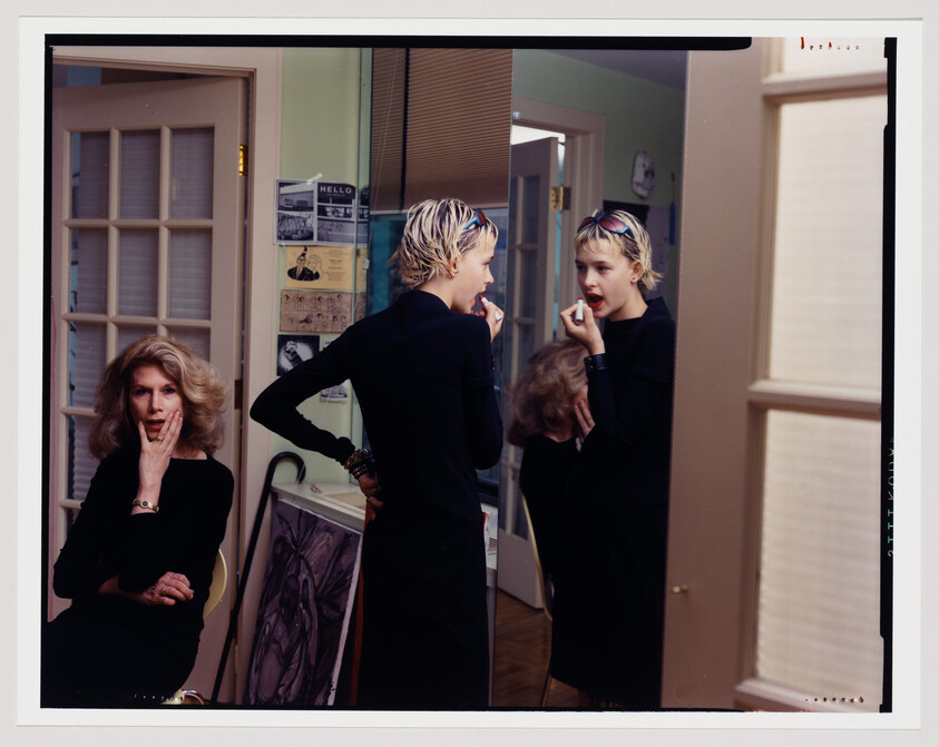 Teen applies lipstick in front of a mirror while an older woman watches with a surprised expression.