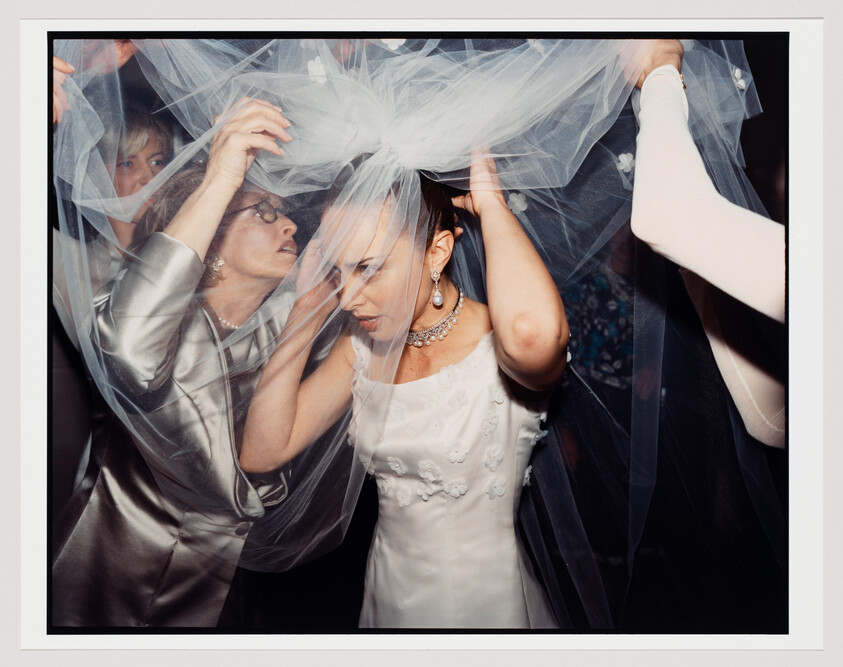 Bride adjusts her veil while family members help position it over her head.
