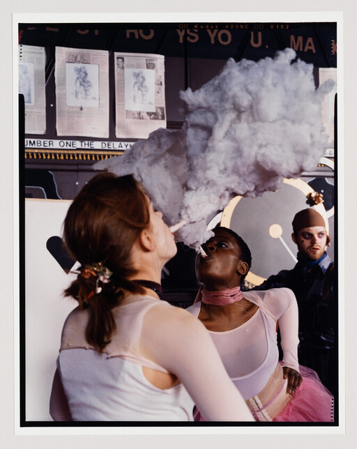 Two performers exhale a large cloud of smoke during a theatrical act while a third watches.