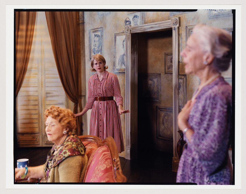 Young woman in a red checked dress stands in a doorway looking concerned while two older women converse.