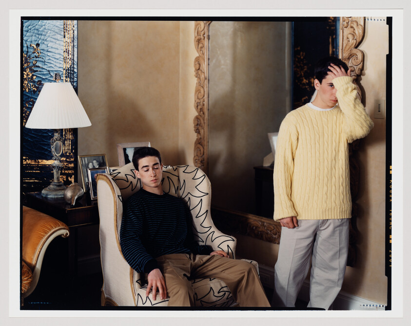 Two young men in a living room, one slumped in a chair and the other standing with hand on his forehead.