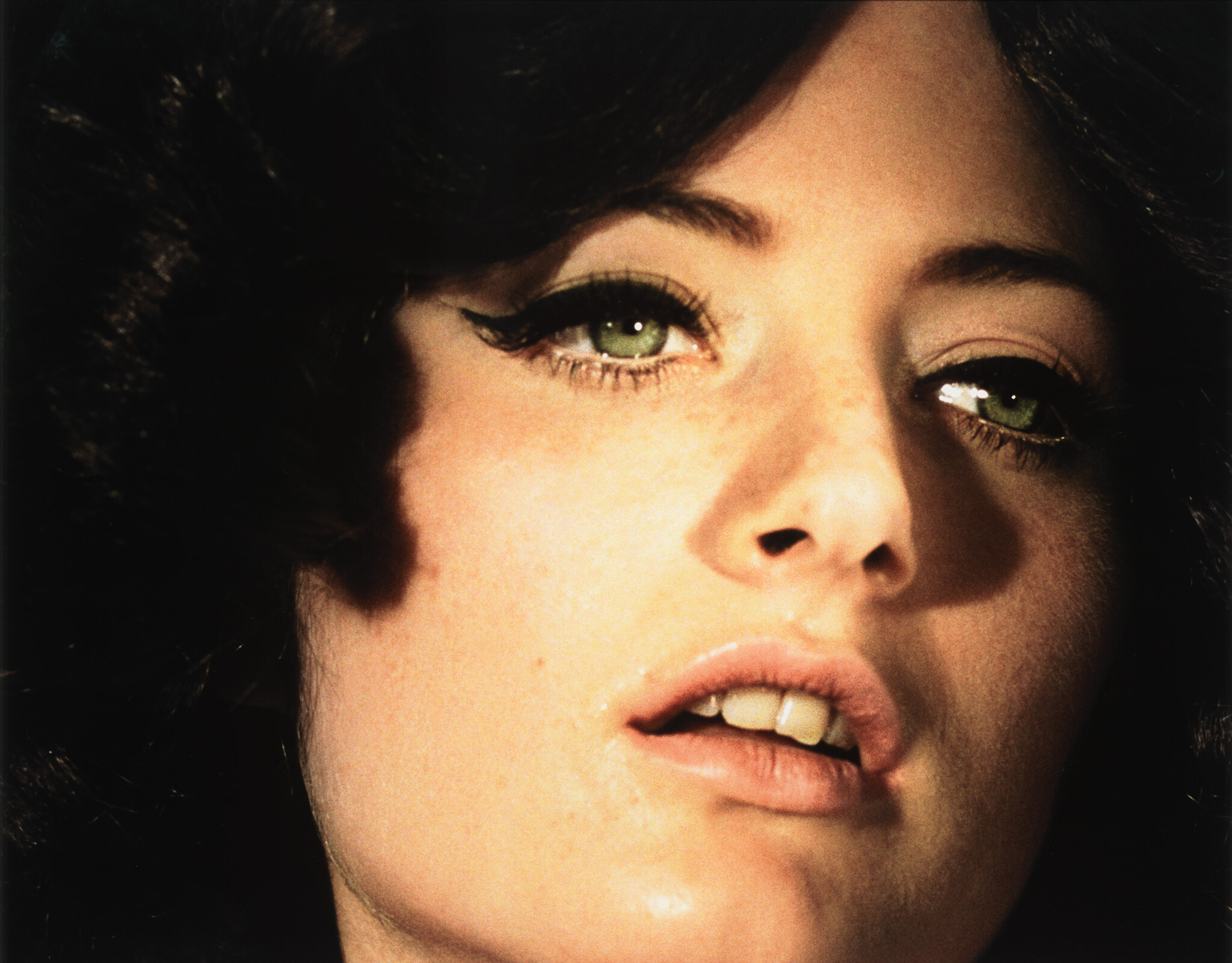Close-up of a woman's face with green eyes, heavy eyeliner, and slightly parted lips.