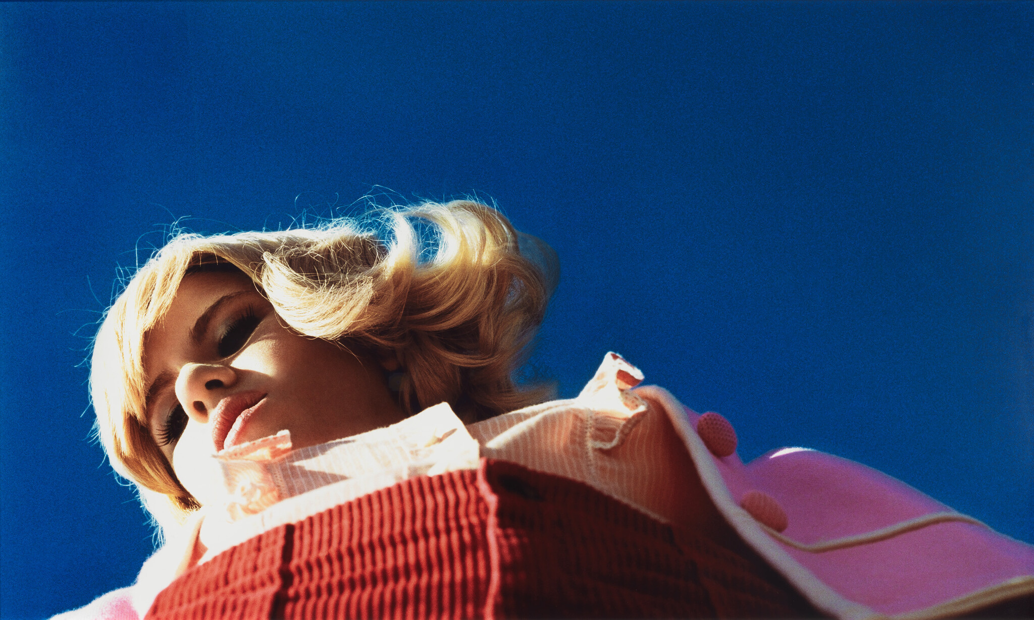 Young woman with short blonde hair looks down against a clear blue sky.