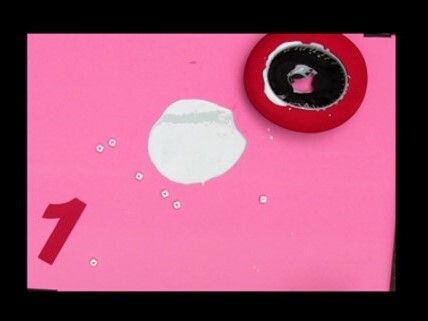 Red and black circular stamp beside a white paint blob on a pink sheet with a red 1.