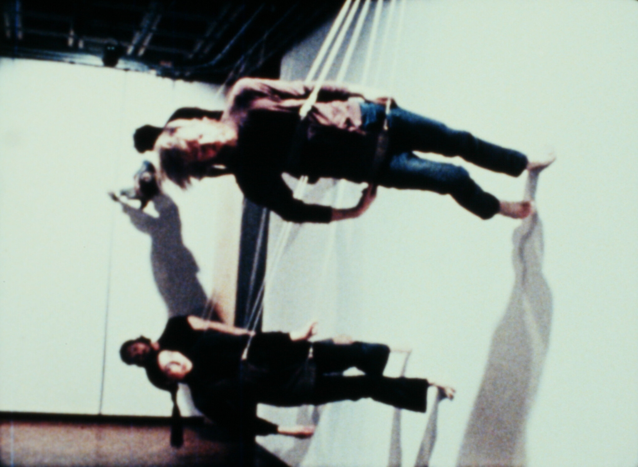 Three people wearing straps stand on narrow platforms while balancing and leaning against each other.