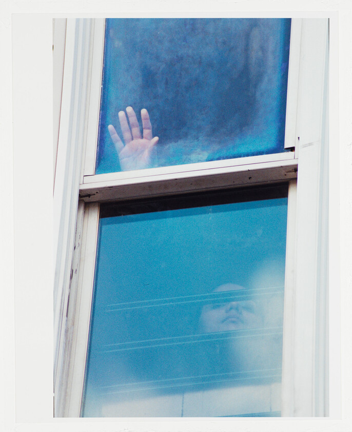 A person looks up through a window while their hand presses against the upper pane.