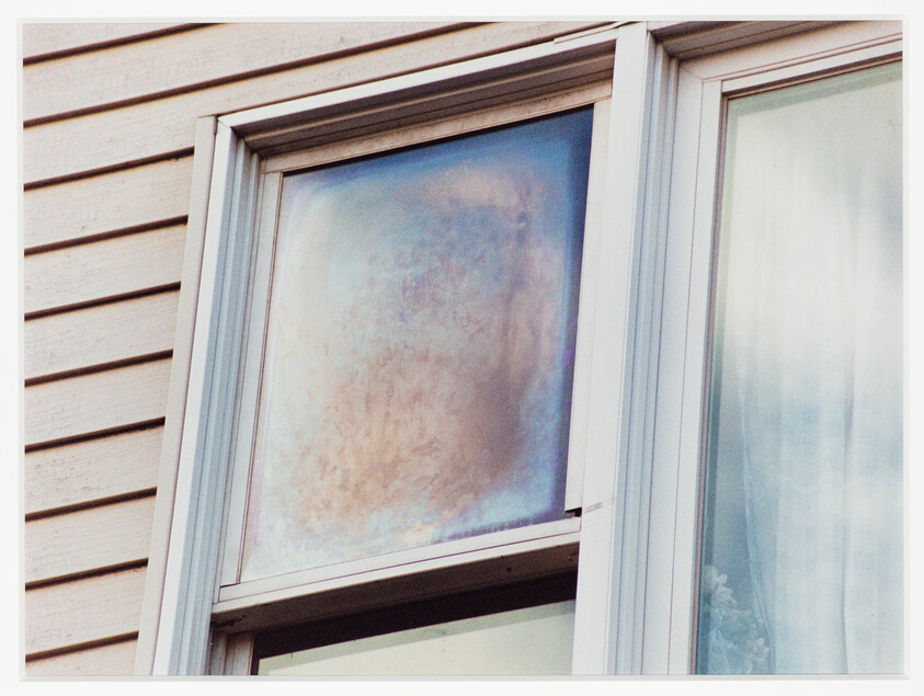 Upper window pane with large iridescent discoloration on a house siding.