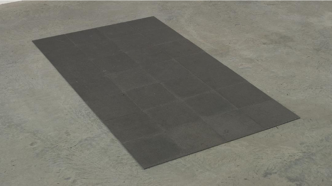 A rectangular black mat lies on a gray concrete floor, creating a stark contrast with the surrounding surface.