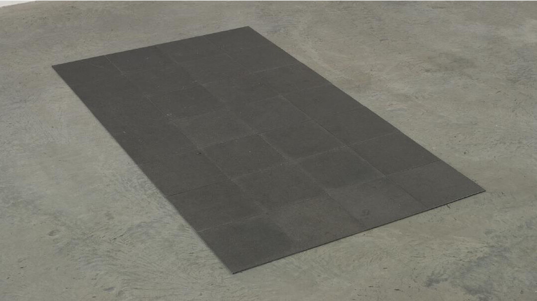 A large, dark rectangular mat lies on a light gray concrete floor.