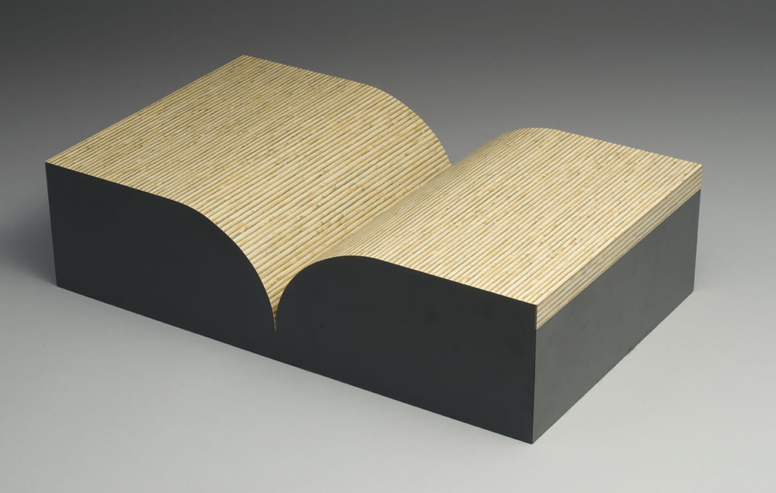 Wooden sculpture resembling an open book with curved pages and striped texture on top.