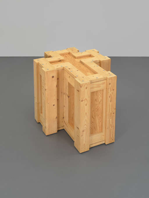 A freestanding wooden crate sculpture assembled from interlocking pine panels forming a cross-shaped top.