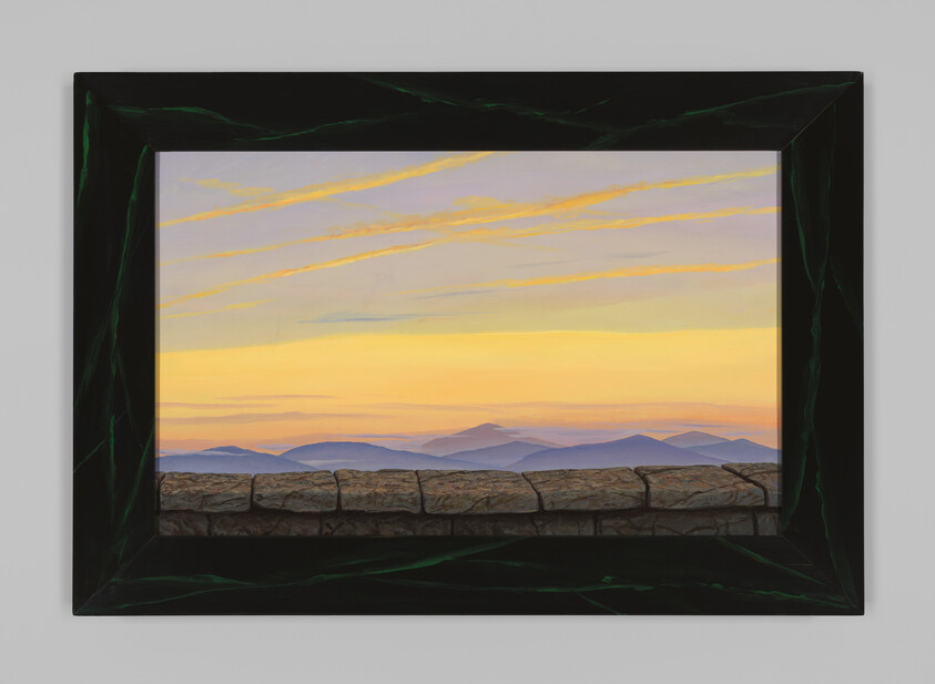 A stone wall frames a view of distant mountains under a yellow and orange sky.