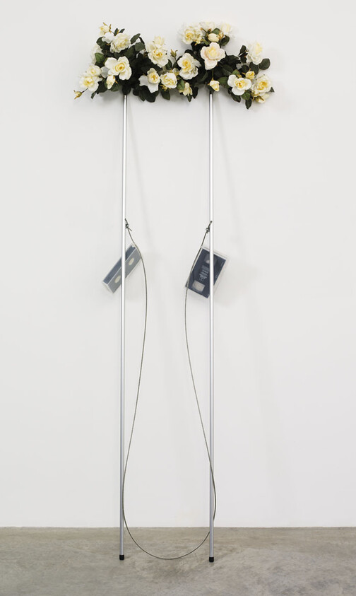 Two tall metal poles topped with white roses hold cassette tapes suspended by wires between them.