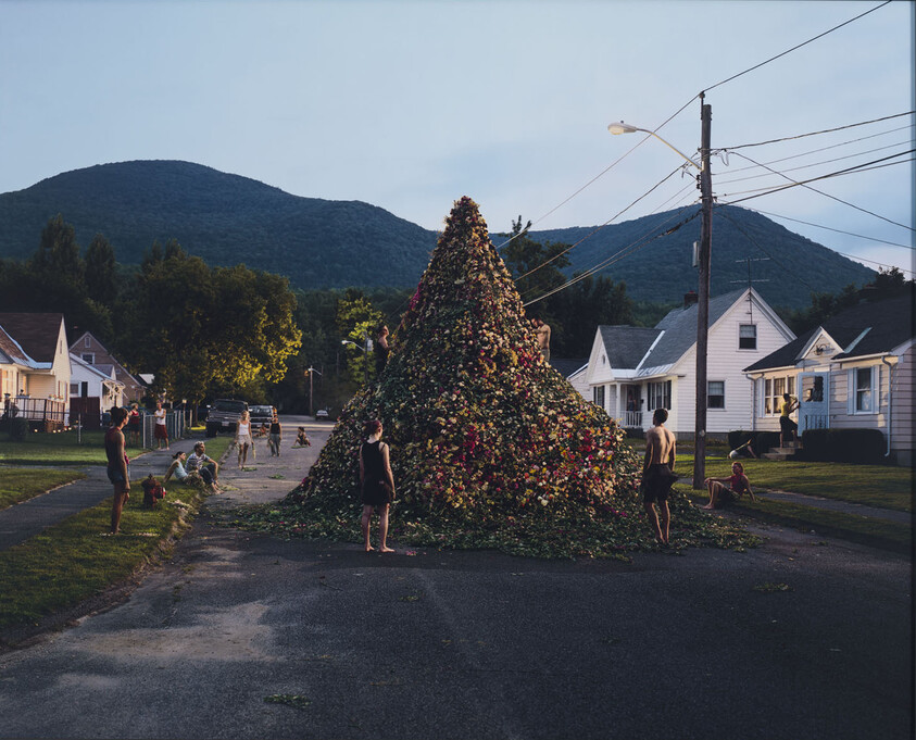 A huge cone of flowers fills the street as neighbors gather and climb around it.