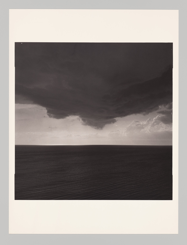 Dramatic black and white seascape with dark storm clouds looming over a calm ocean horizon.