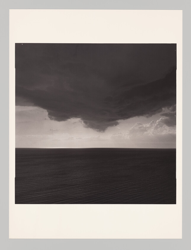 Dark storm cloud hangs over calm ocean horizon before an approaching storm.
