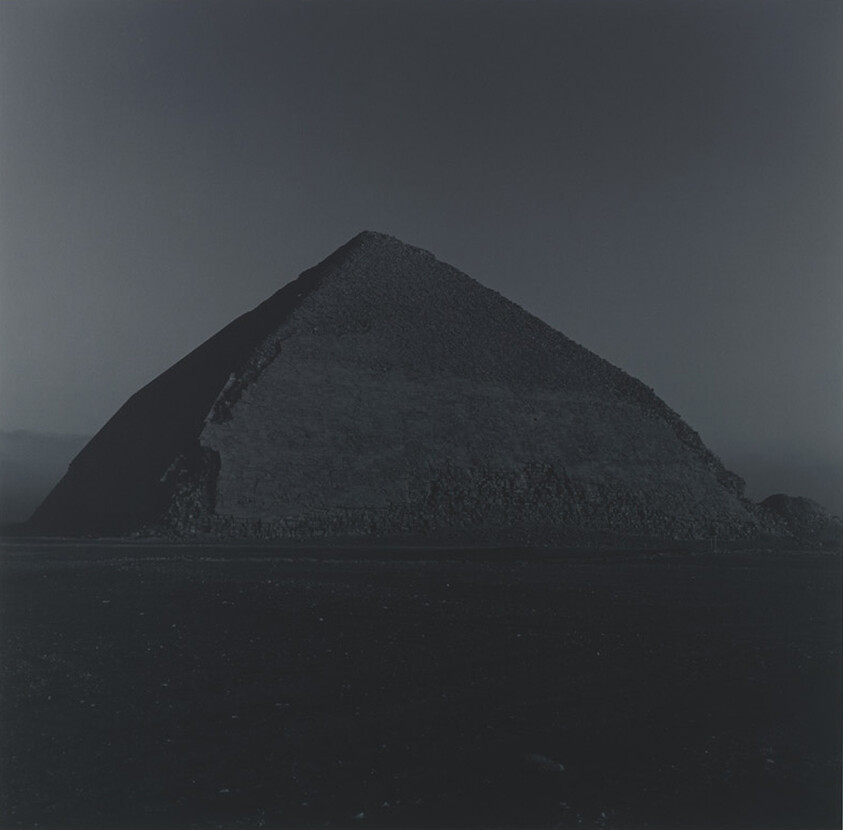 A dark, partially eroded pyramid stands alone against a dim, clear night sky.