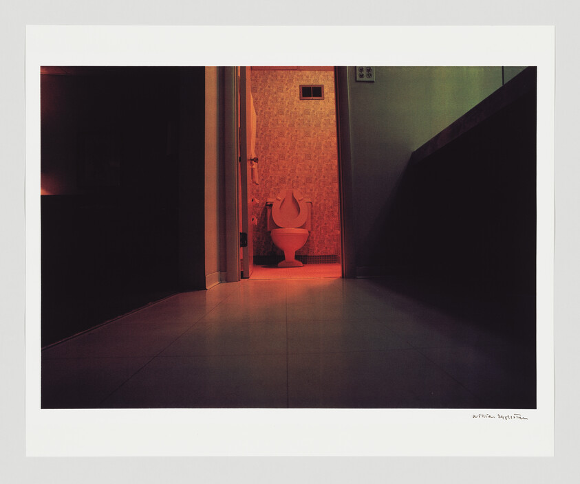 A toilet with the seat raised is seen through an open bathroom door, lit by a red light.