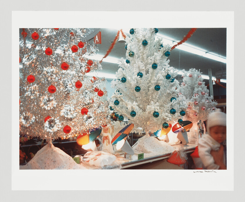Several decorated artificial Christmas trees with colorful ornaments and display lamps on a store counter.