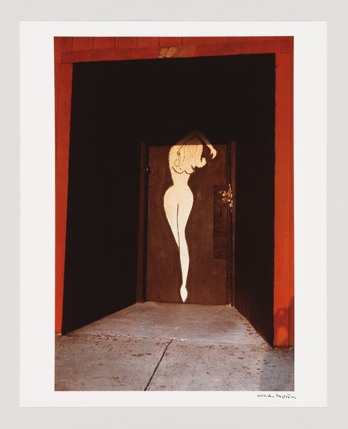 A dark doorway framed in red shows a tall white painted silhouette of a nude woman.