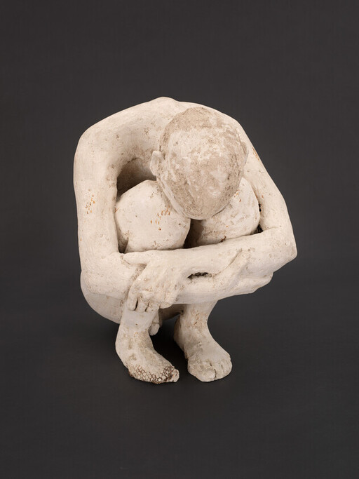 A white sculpture of a crouching person with head bowed and arms wrapped around knees.