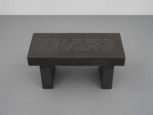 Dark rectangular stone bench with engraved poetic text across its top, standing on two sturdy legs.