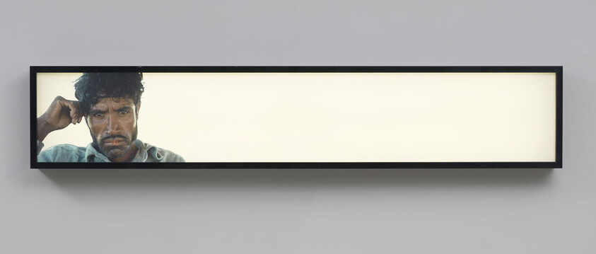 Long illuminated horizontal frame showing a tired man resting his head on his hand at left.