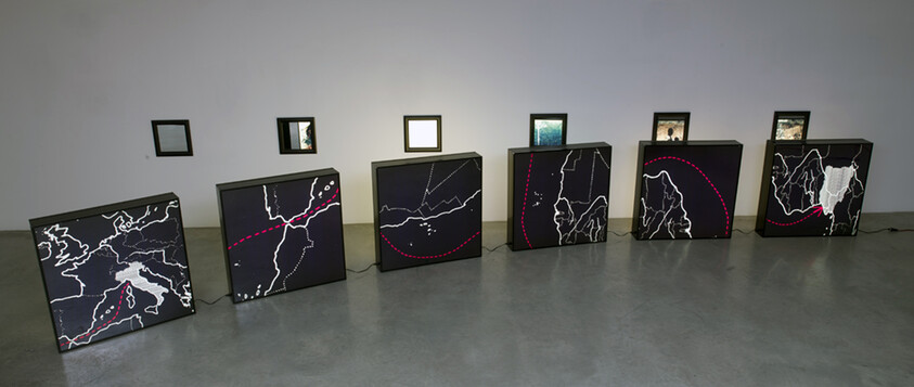 Six illuminated black panels show white map lines and red dotted routes arranged along a gallery wall.