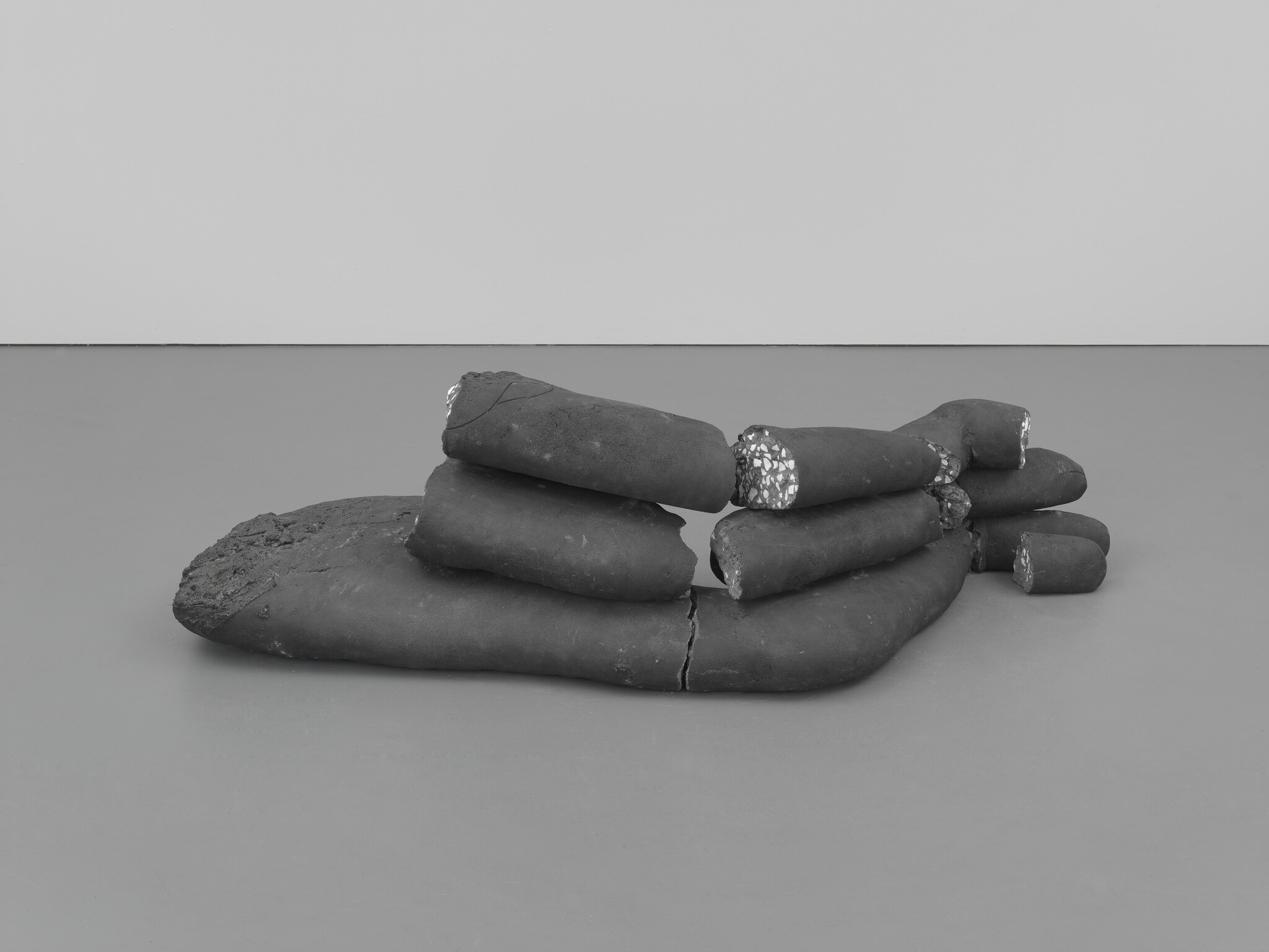 A low pile of dark, sausage-shaped clay sculptures with several broken ends showing speckled interior.