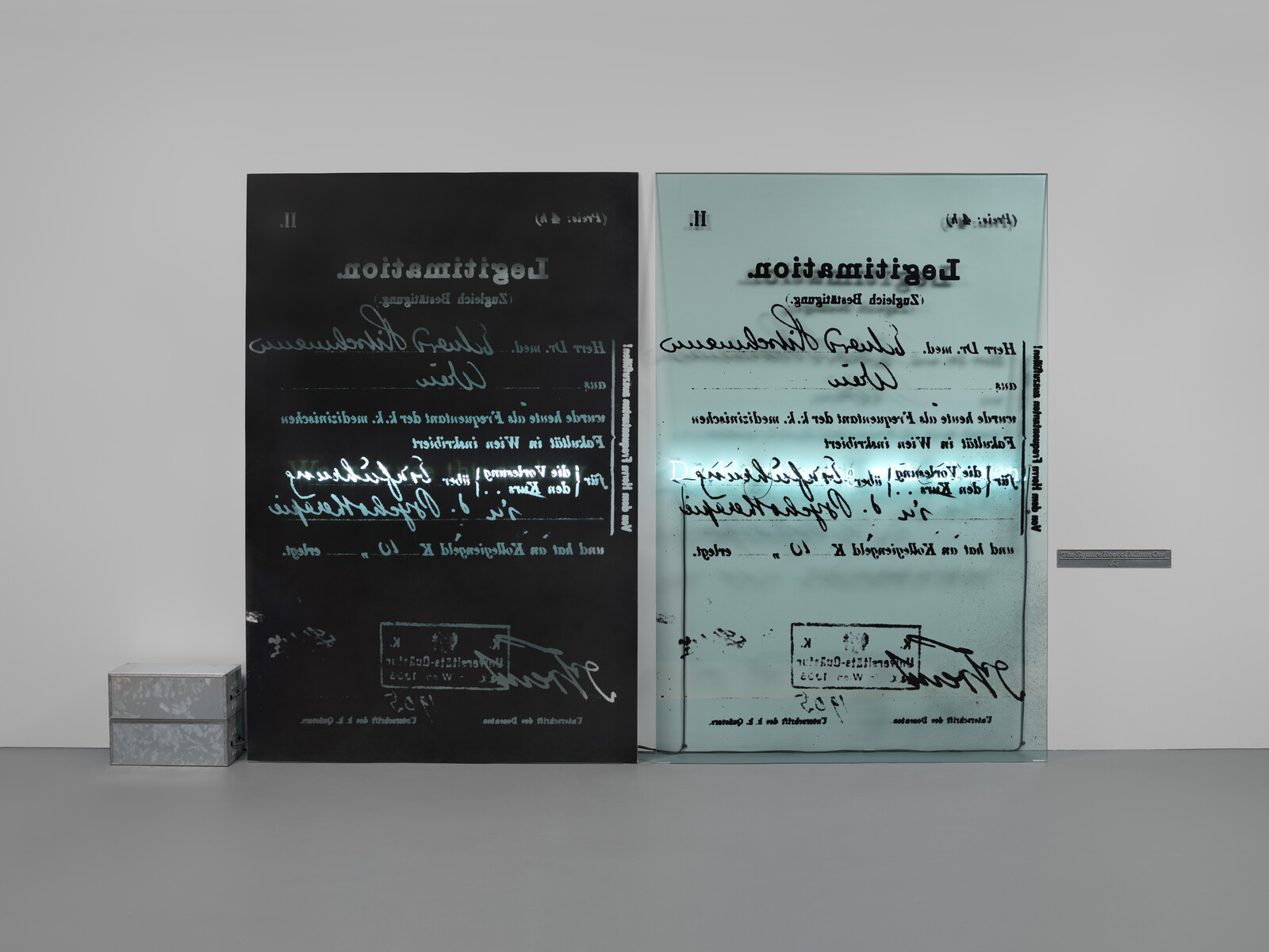 Two large glass panels with reversed handwritten documents lean against a wall beside stacked metal boxes.