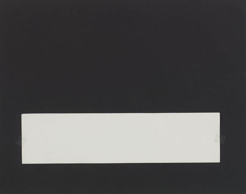 A long white rectangular strip taped to a black background near the bottom edge.