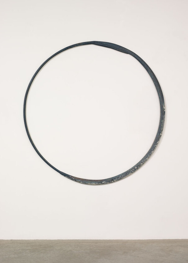 A large weathered metal hoop mounted on a white wall above the floor.