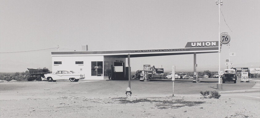 A vintage Union 76 gas station with pumps and classic cars parked under the canopy.