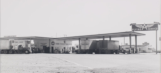 A truck stop canopy with multiple semi-trucks parked and a large vintage service sign.