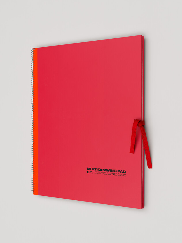 A marron sketchbook with bright red binding is closed with a red ribbon