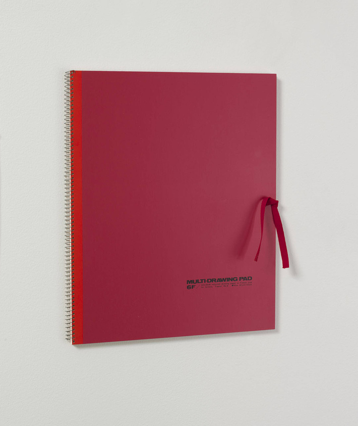 A marron sketchbook with bright red binding is closed with a red ribbon