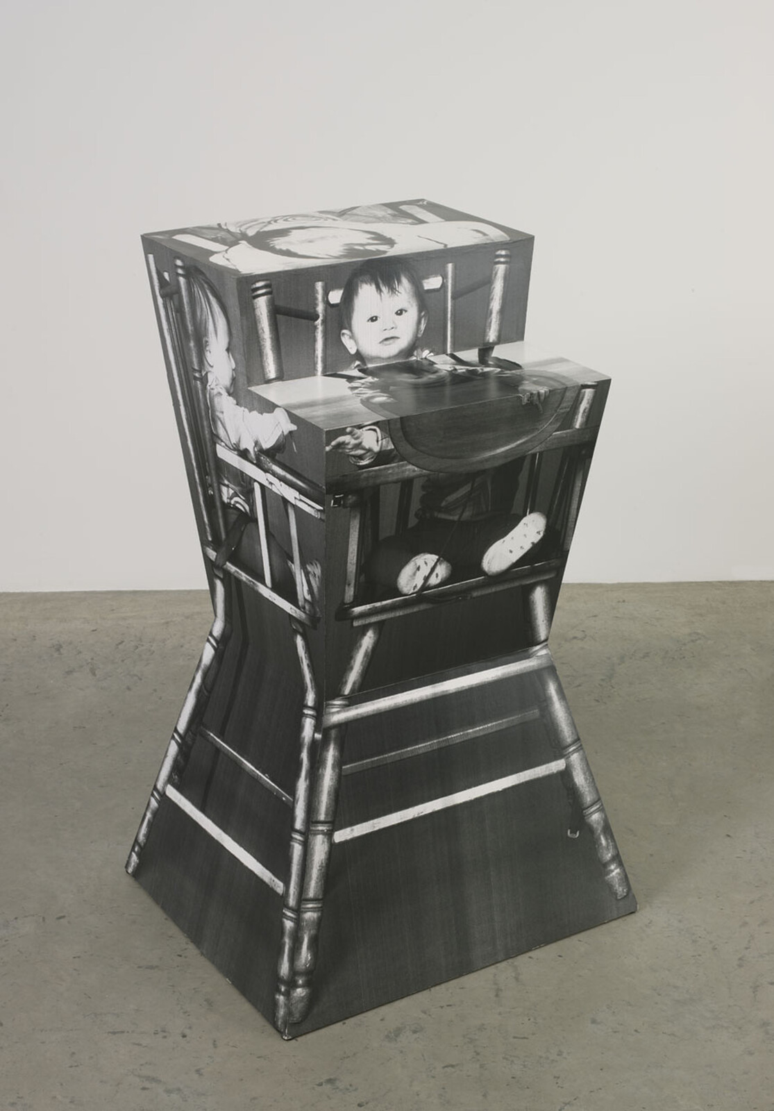 A sculpture shaped like a high chair, featuring black-and-white images of a baby on its surfaces.
