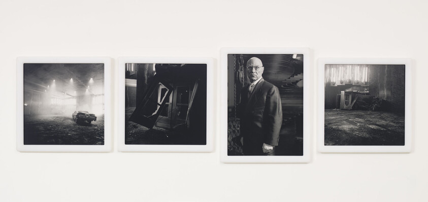 Four framed black-and-white photographs on a white wall, one showing a man in a suit.