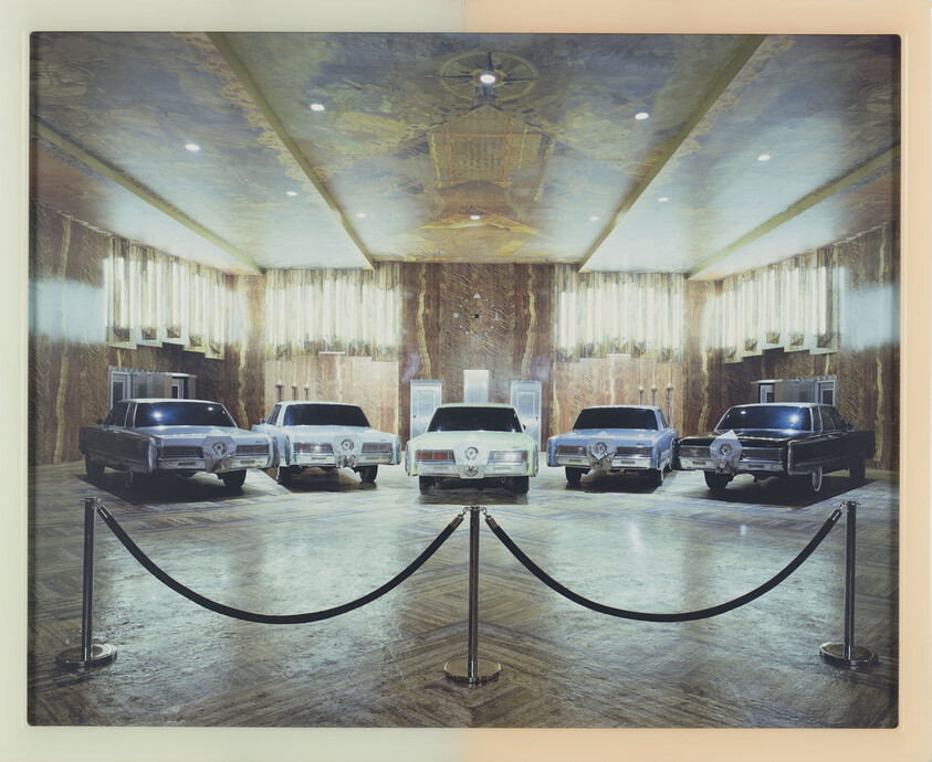 Five vintage limousines displayed in an ornate hall behind stanchion ropes.