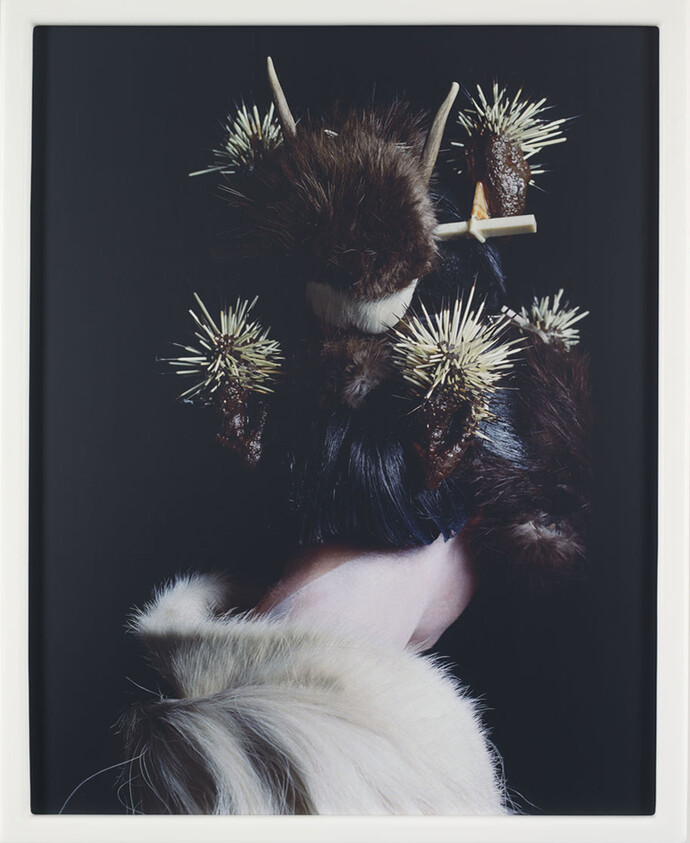 A person holds a furry, spiky object with horns, set against a dark background.