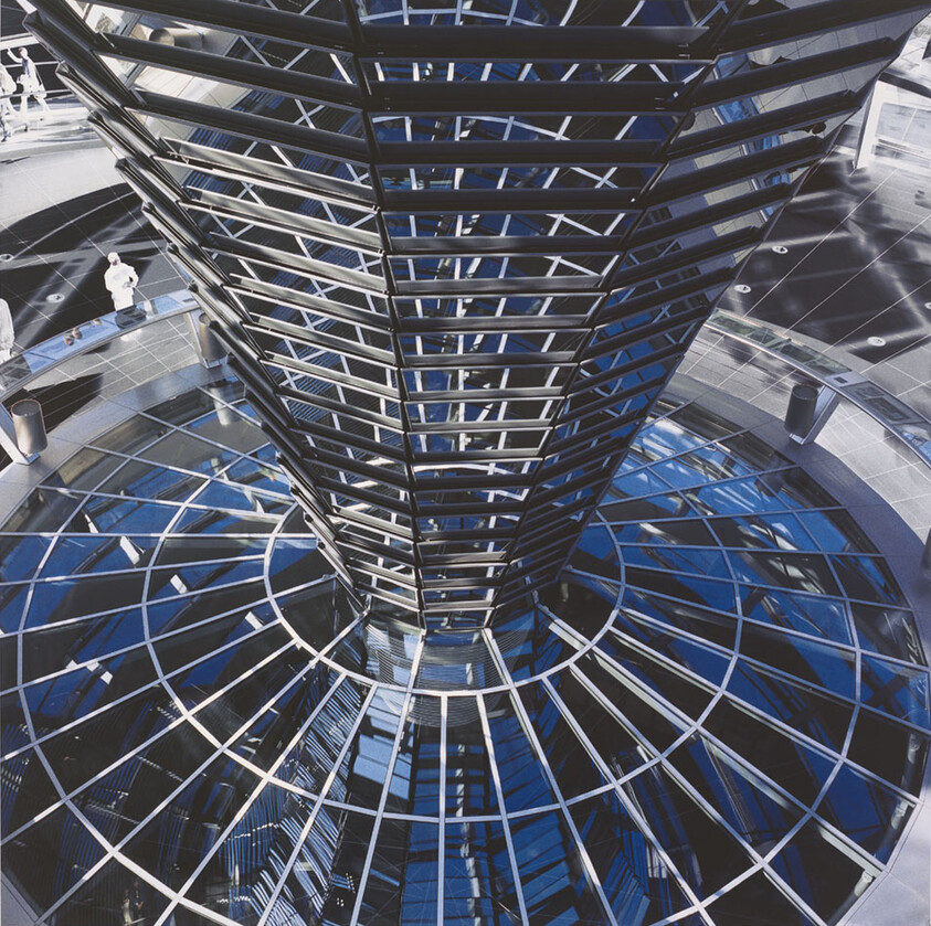 Looking down at a modern glass and steel spiral structure with people walking around it.