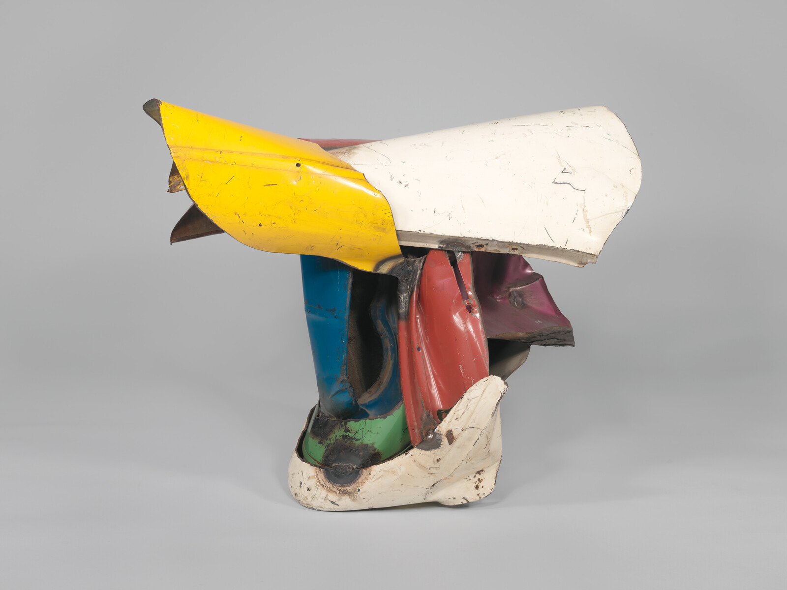 Colorful crushed automobile panels assembled into a compact abstract sculpture resembling stacked metal fragments.