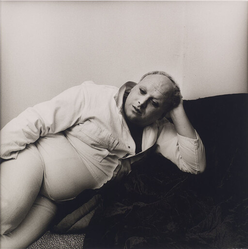 A person in light clothing reclines on a couch, resting their head on their hand.