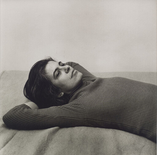 A person lies on a bed with arms behind their head, looking calmly toward the camera.