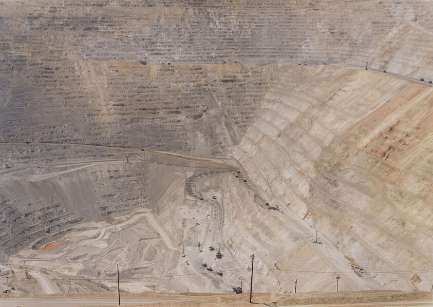 Huge terraced open-pit mine with winding haul roads and small trucks working on the benches.