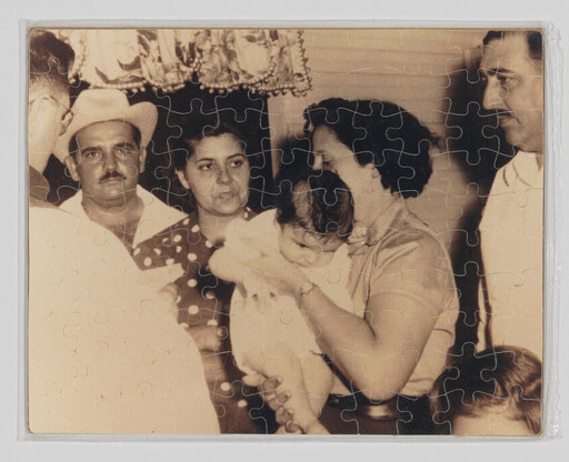 A woman holds a small baby while family members look on in a sepia-toned gathering.