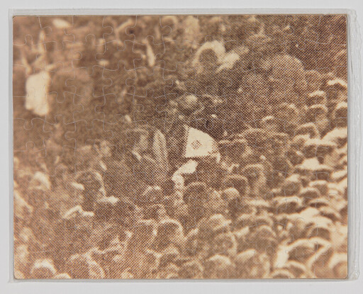 A crowded group of people with one person holding a small white flag above the heads.