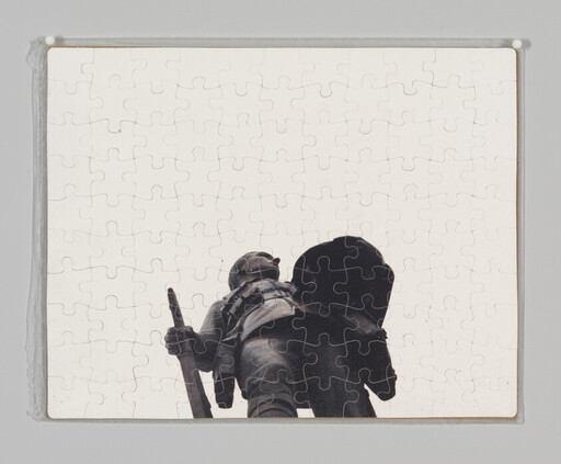 A completed jigsaw puzzle shows a soldier statue viewed from below holding a rifle and helmet.
