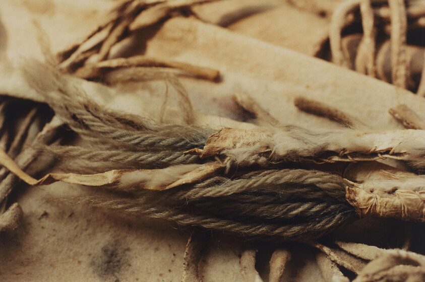 Close-up of frayed braided rope and worn leather fringe with dusty, aged texture.