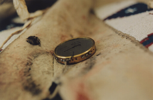 A small round brass coin rests on stained, worn fabric with visible stitching and discoloration.
